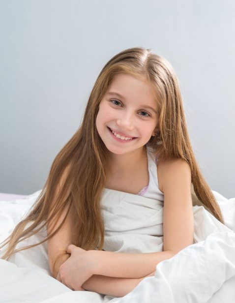 kid with long hair sitting in bed